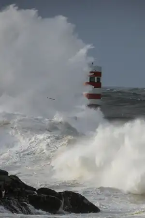 Onda alta a bater num rochedo que tem um farol vermelho.